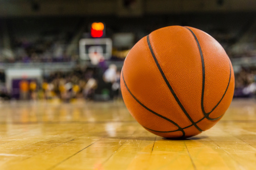 A basketball lies on the dusty hardwood court of a college hoops arena during a break in the action.